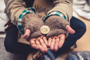 homeless person's hands with Bitcoin token being held